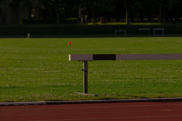 A single hurdle positioned on a track, prominently featuring a red flag flapping in the background,...