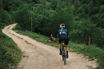Obraz premium Female cyclist rides gravel bike down scenic country road. Stunning natural landscape. Perfect for travel, adventure, and active lifestyle concepts.