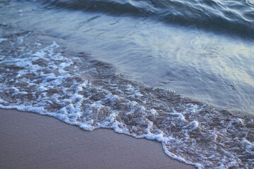 Gentle ocean wave washes over the sandy beach, leaving a delicate pattern of foam. Captures the peaceful rhythm of the sea, perfect for coastal nature themes, travel, and relaxing design concepts