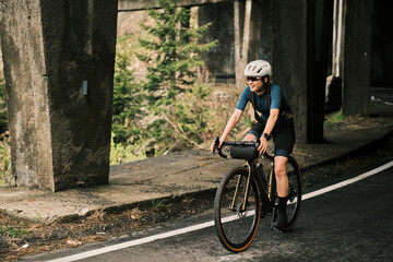 Smiling woman cycling on a gravel bike under a bridge.  Adventure, freedom, and outdoor activity....