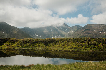 Serene mountain lake reflecting the majestic peaks and fluffy clouds. A tranquil scene of nature's...