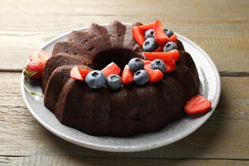 Tasty chocolate bundt cake with berries on wooden table, closeup