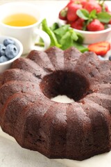Tasty chocolate bundt cake, tea and berries on light table, closeup