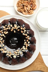 Delicious chocolate bundt cake with nuts and glass of milk on white wooden table, flat lay