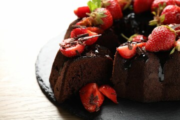 Delicious chocolate bundt cake with strawberries on wooden table, closeup