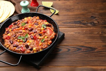Tasty chili con carne in baking dish and flatbread on wooden table, closeup. Space for text