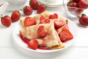 Delicious crepes with strawberries and sauce on white wooden table, closeup