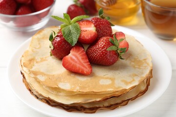 Delicious crepes with strawberries, honey, mint and tea on white table, closeup