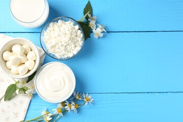 Different fresh dairy products and flowers on light blue wooden table, flat lay. Space for text