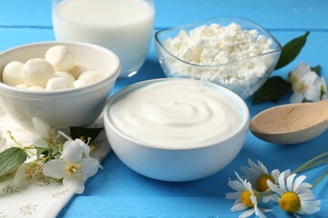 Different fresh dairy products and flowers on light blue wooden table, closeup