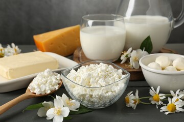 Fresh dairy products and flowers on grey wooden table against textured background, closeup