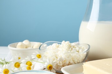 Fresh dairy products and flowers on table against light blue background, closeup