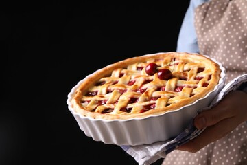 Woman holding tasty cherry pie on black background, closeup