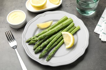 Tasty cooked asparagus served with lemon on grey table, closeup