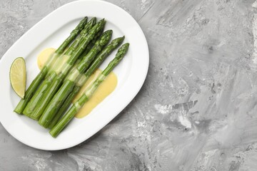 Tasty cooked asparagus served with sauce and lime on grey textured table, top view. Space for text