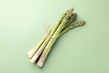 Tied raw asparagus on green background, top view