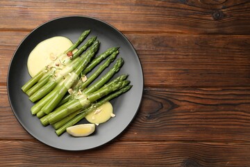 Tasty cooked asparagus served with sauce on wooden table, top view. Space for text