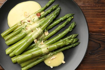 Tasty cooked asparagus served with sauce on wooden table, top view