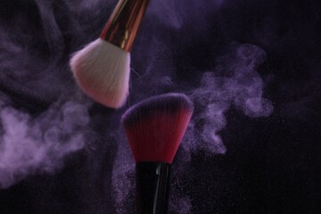 Makeup brushes with purple eye shadow on black background, closeup