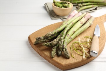 Fresh raw asparagus spears and knife on white wooden table, closeup. Space for text