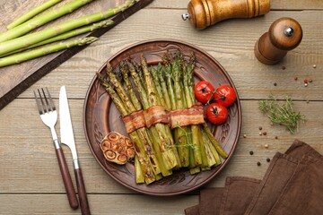 Tasty cooked asparagus served with bacon and spices on wooden table, flat lay