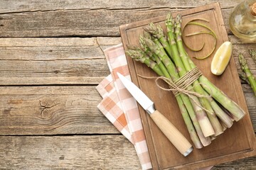 Fresh raw asparagus spears, knife, oil and lemon on wooden table, flat lay. Space for text