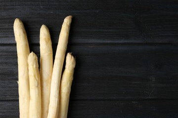Raw white asparagus spears on black wooden table, flat lay. Space for text