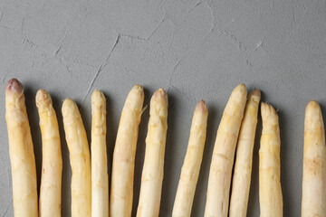 Raw white asparagus spears on grey textured table, flat lay. Space for text