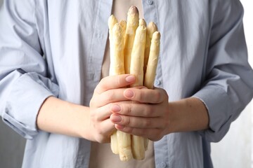 Woman with raw white asparagus spears on grey background, closeup