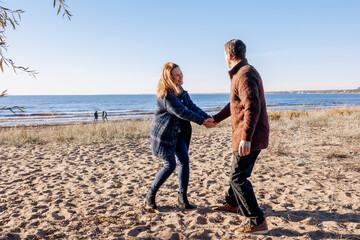 Loving couple walks on beach along sea on sunny autumn day. Weekend and lifestyle concept. High quality photo