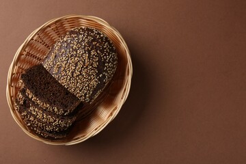 Fresh rye bread with seeds in wicker basket on brown background, top view. Space for text
