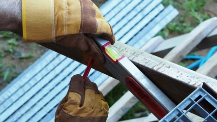 Close-up of gloved hands holding a level tool, ensuring precision in construction work, with a background of wooden beams and a clear blue sky, showcasing craftsmanship and attention to detail