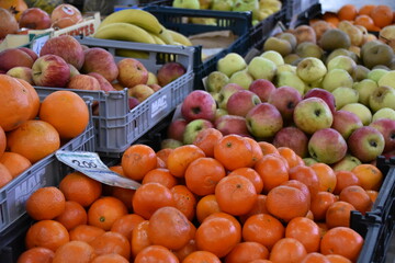 A vibrant fruit market display with fresh, shiny tangerines in the foreground and a mix of red and green apples in the background.