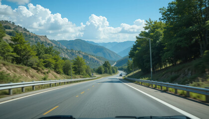 A highway stretches through a mountainous landscape under a partly cloudy sky, with trees lining the roadside.