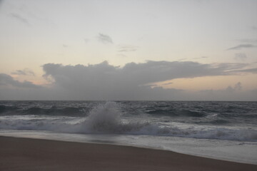 Waves crash onto the shore at Praia do Norte in Nazaré, Portugal, under a cloudy sunset sky—famous for its giant waves and dramatic ocean views.