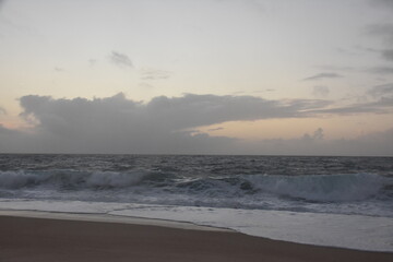 Waves crash onto the shore at Praia do Norte in Nazaré, Portugal, under a cloudy sunset sky—famous for its giant waves and dramatic ocean views.