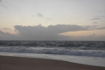 Waves crash onto the shore at Praia do Norte in Nazaré, Portugal, under a cloudy sunset sky—famous for its giant waves and dramatic ocean views.