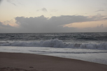Waves crash onto the shore at Praia do Norte in Nazaré, Portugal, under a cloudy sunset sky—famous for its giant waves and dramatic ocean views.