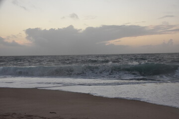 Waves crash onto the shore at Praia do Norte in Nazaré, Portugal, under a cloudy sunset sky—famous for its giant waves and dramatic ocean views.