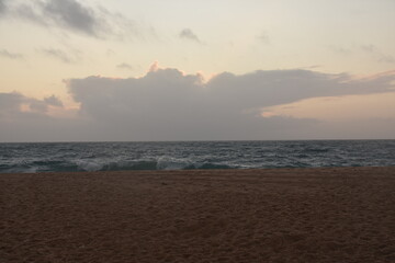 Waves crash onto the shore at Praia do Norte in Nazaré, Portugal, under a cloudy sunset...