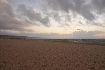 Waves crash onto the shore at Praia do Norte in Nazaré, Portugal, under a cloudy sunset...