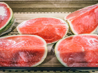 A bunch of red watermelon slices are on a wooden shelf