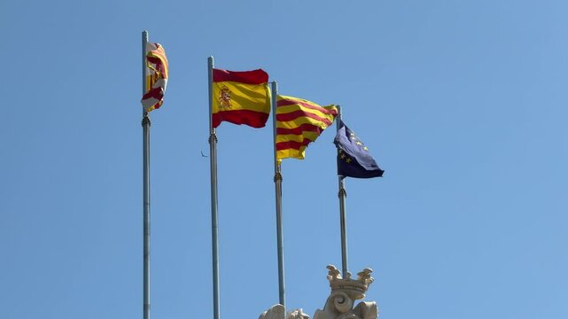 Flags of Spain, the European Union, Barcelona, and Catalonia waving together in the wind.