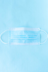 Vertical shot of blue disposable surgical mask placed against a similarly blue background representing medical protection.