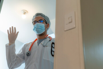 Healthcare professional standing at the entrance and greeting with hand, wearing protective equipment including mask, gloves, and hairnet, symbolizing approachability, care, and safety.