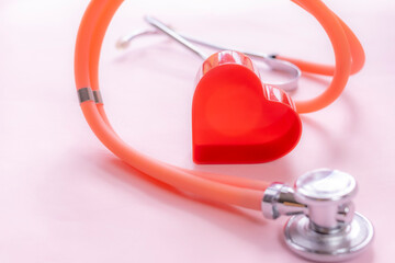 Medical-themed composition featuring a red heart-shaped object next to an orange stethoscope on pink background. Perfect for illustrating healthcare, diagnostics, or cardiology-related concepts.