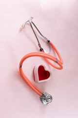 Medical-themed composition featuring a red heart-shaped object next to an orange stethoscope on pink background. Perfect for illustrating healthcare, diagnostics, or cardiology-related concepts.