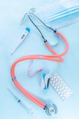 Vertical shot of medical tools and accessories, including a stethoscope, pills, medical mask and electronic thermometer, arranged on a light background, symbolizing healthcare, diagnosis, and medical 