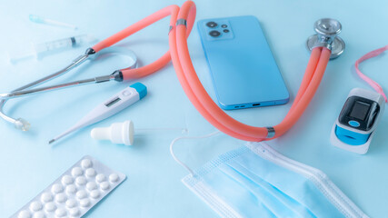 Smartphone with some medical tools and accessories, including a stethoscope, pills, medical mask and electronic thermometer.