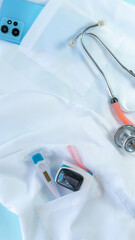 Smartphone with some medical tools and accessories, including a stethoscope, medical mask and electronic thermometer in medical coat pockets